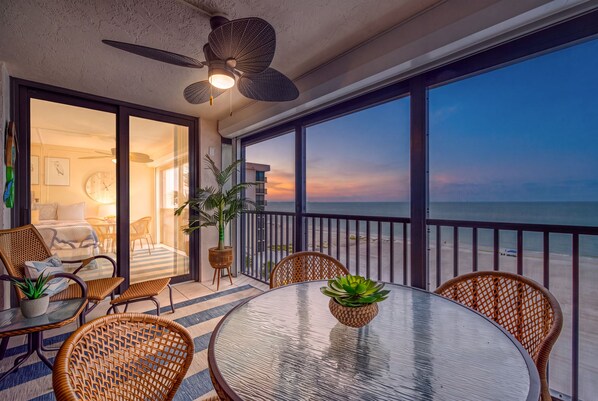 A balcony with a glass table, wicker chairs, and potted plants.
