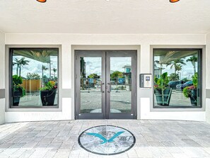 A hotel entrance with a glass door, potted plants, and a tiled floor. - Beachfront Getaway at Caper Beach Club #903 | Private Chiller/Heated Pool (Fort Myers Beach)