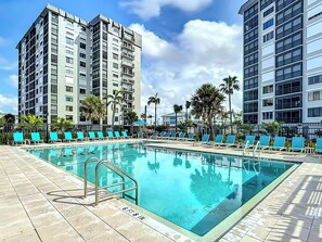 A swimming pool with blue lounge chairs and a metal ladder, surrounded by tall buildings and palm trees. - Beachfront Getaway at Caper Beach Club #903 | Private Chiller/Heated Pool (Fort Myers Beach)