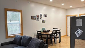 Una sala de estar moderna con un sofá gris, una mesa de comedor con sillas y un refrigerador con un letrero para mascotas.
