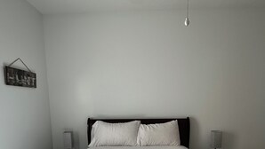 Une chambre avec un grand lit, deux tables de chevet avec des lampes, un luminaire fixé au mur et un petit panneau accroché au mur.