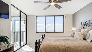 A bedroom with a large window, a ceiling fan, a bed with a quilt, and a nightstand with a lamp.