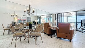 A spacious living area with a dining set, comfortable seating, and large windows offering a view.