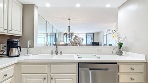 A modern kitchen with white cabinetry, a stainless steel dishwasher, a coffee maker, and a chandelier.
