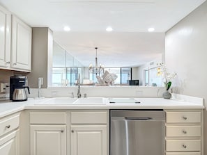 A modern kitchen with white cabinetry, a stainless steel dishwasher, a coffee maker, and a chandelier.