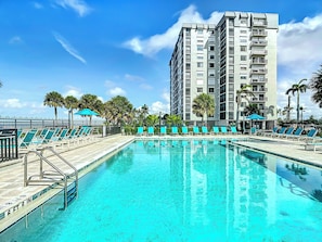 Una piscina con sillones reclinables y un edificio alto al fondo.