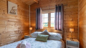 A wooden cabin bedroom with a bed, pillows, a nightstand, and a window with curtains. - Moor View (Oak Tree Lane)
Gorgeous rustic charm (Okehampton)