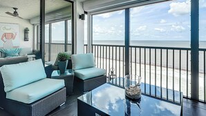 Un balcón con mobiliario de mimbre, una mesa de vidrio y vista a la playa.