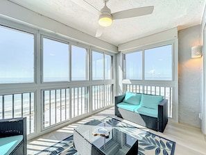 A sunlit room with large windows, a ceiling fan, and a wicker sofa with cushions. - Beachfront Getaway at Caper Beach Club #1105 | Private Chiller/Heated Pool (Fort Myers Beach)