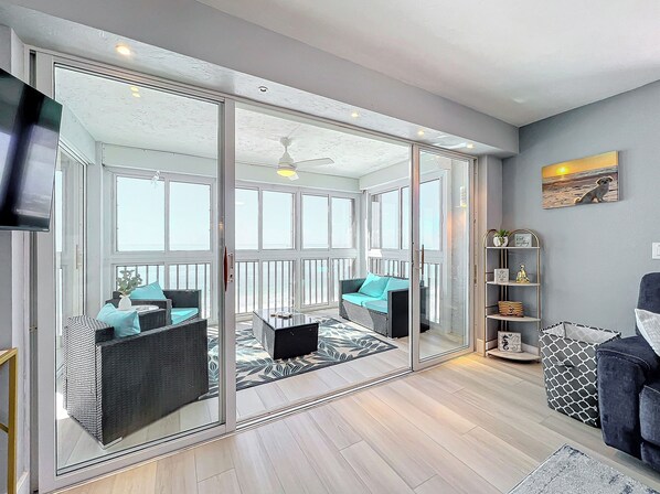 A spacious living area with a sliding glass door leading to a balcony, furnished with wicker sofas and a patterned rug. - Beachfront Getaway at Caper Beach Club #1105 | Private Chiller/Heated Pool (Fort Myers Beach)