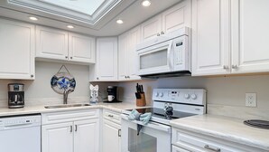Una cocina moderna con armarios blancos, microondas integrado, estufa y cafetera.