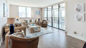 Ein geräumiges Wohnzimmer mit einem großen Schiebeglastür, die auf einen Außenbalkon führt, mit einer Sofagarnitur, einem Couchtisch und einer Lampe.