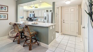 A kitchen with white cabinets, a microwave, and a refrigerator. There is a dining area with two chairs and a table.