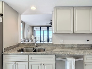 A kitchen with granite countertops, stainless steel sink, and white cabinetry.