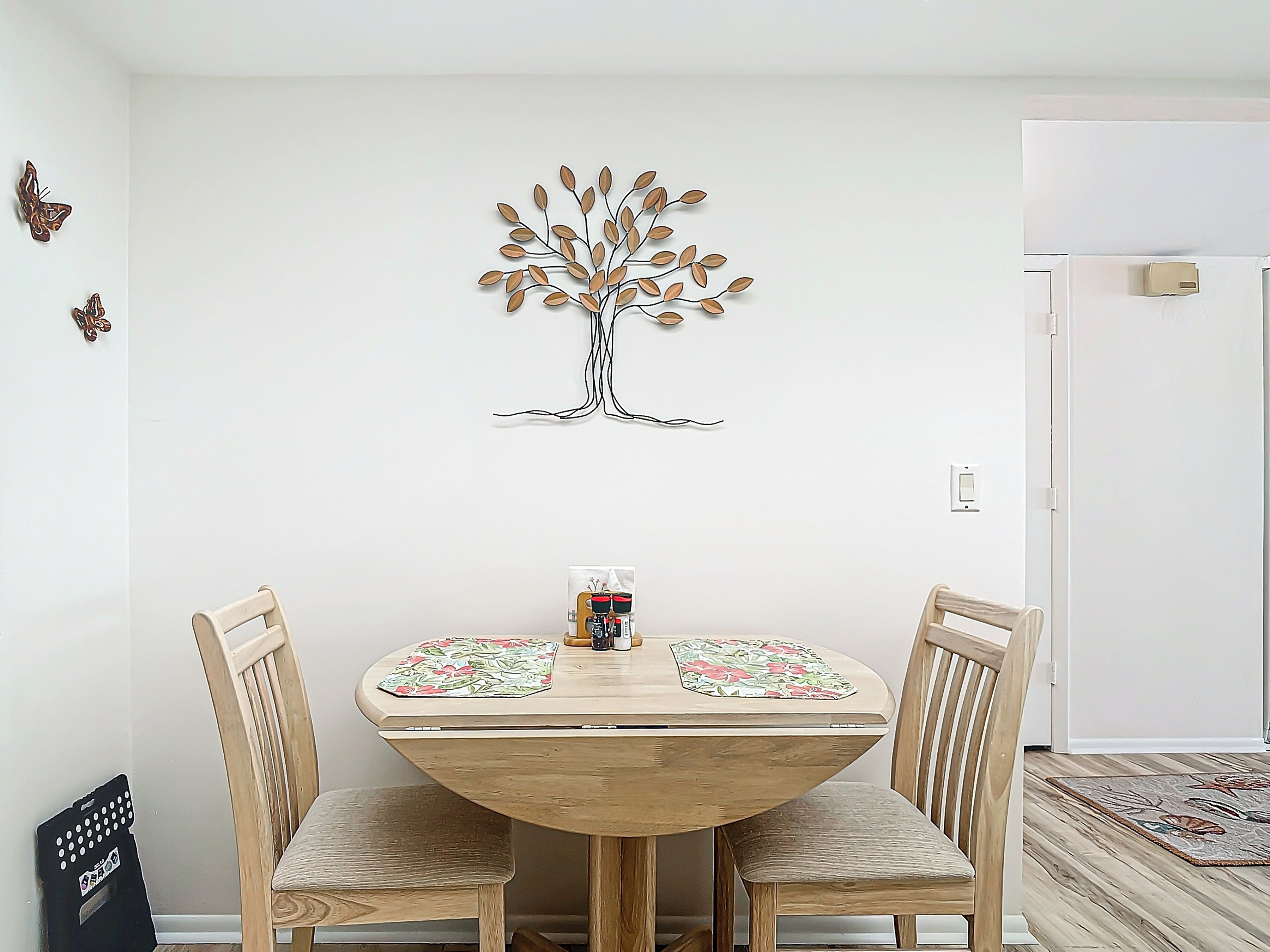 A dining area with a round wooden table, two chairs, and a wall-mounted tree decoration.