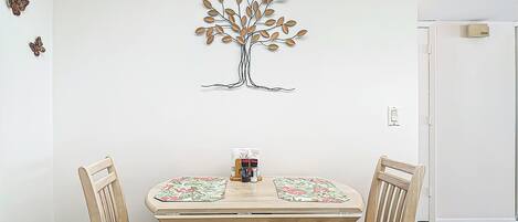 A dining area with a round wooden table, two chairs, and a wall-mounted tree decoration.
