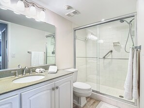A modern bathroom with a glass-enclosed shower, a large mirror, and a vanity with a sink and cabinet.