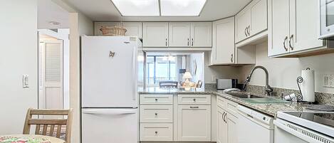 Una cocina compacta con armarios blancos, un refrigerador empotrado, microondas y lavavajillas.