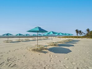 Una playa con filas de sillas de baño y sombrillas, cielo despejado y palmeras.