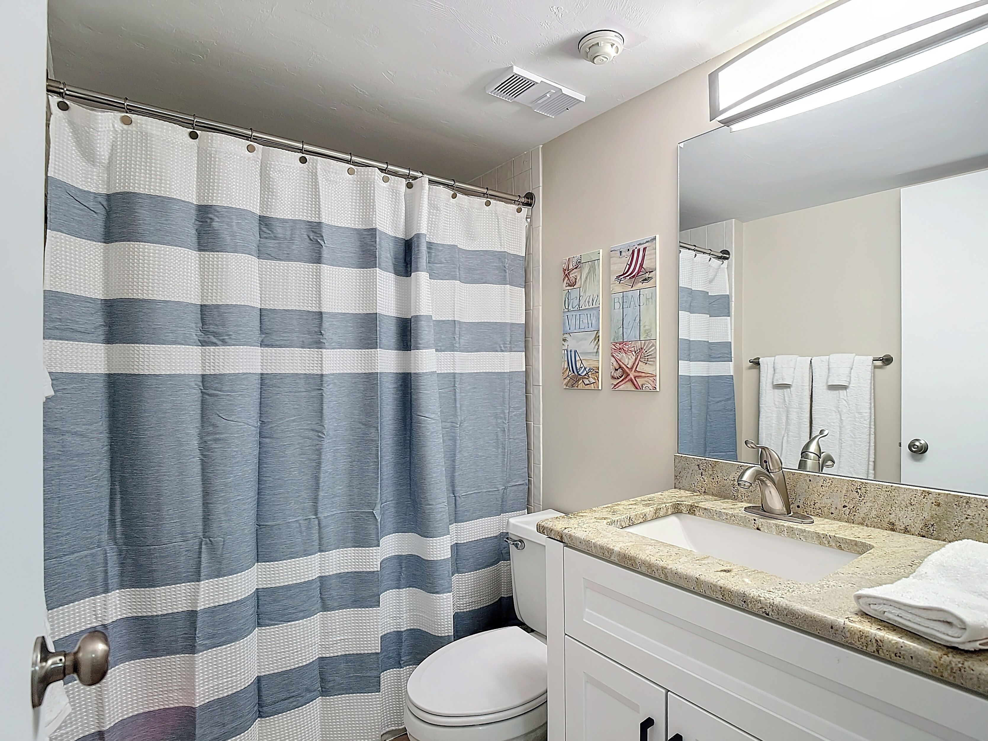 Une salle de bain avec un rideau de douche à rayures, un lavabo doté d’un plan de travail en granit et des toilettes.