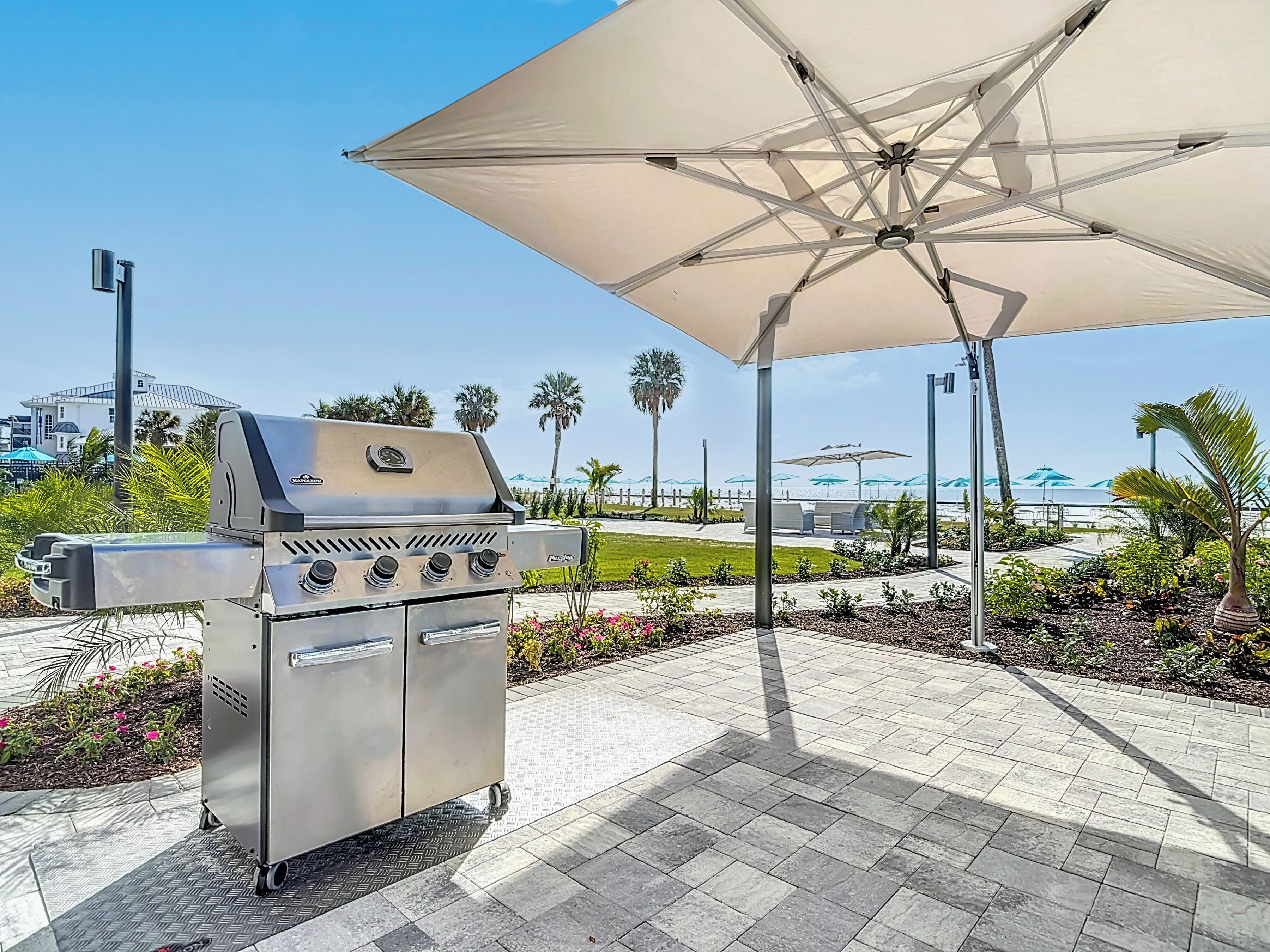 Area barbecue esterna con patio, ombrellone e vista sulla spiaggia.