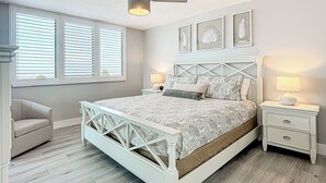 A bedroom with a bed, a nightstand, a chair, a ceiling fan, and framed artwork on the wall.