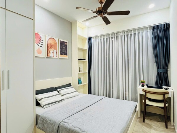 A bedroom with a bed, a desk, a chair, a ceiling fan, and a window with curtains.
