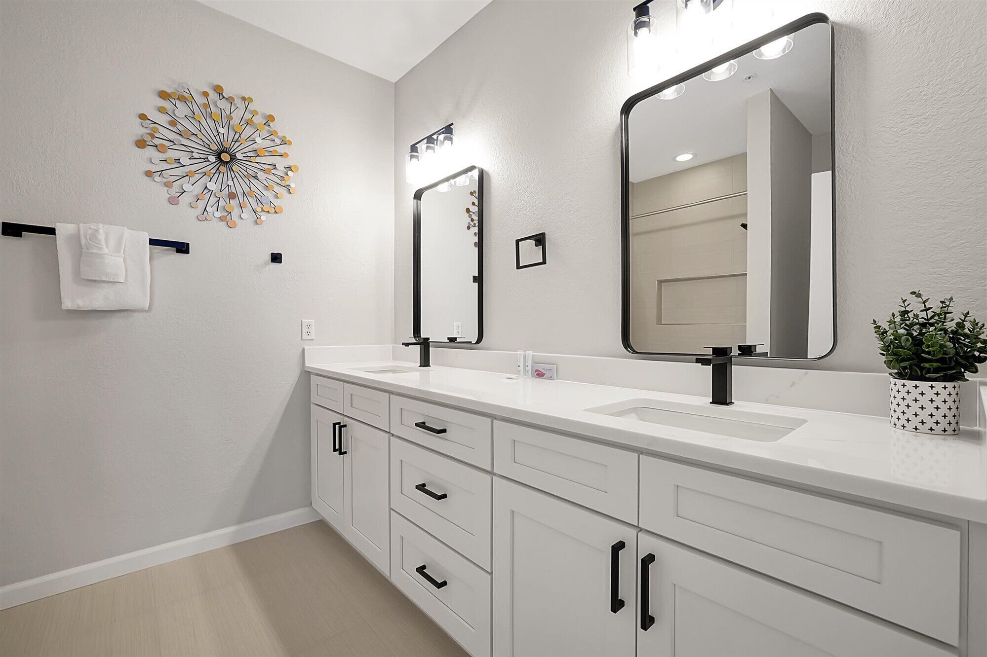 A modern bathroom with a white vanity, two mirrors, and a decorative wall piece.