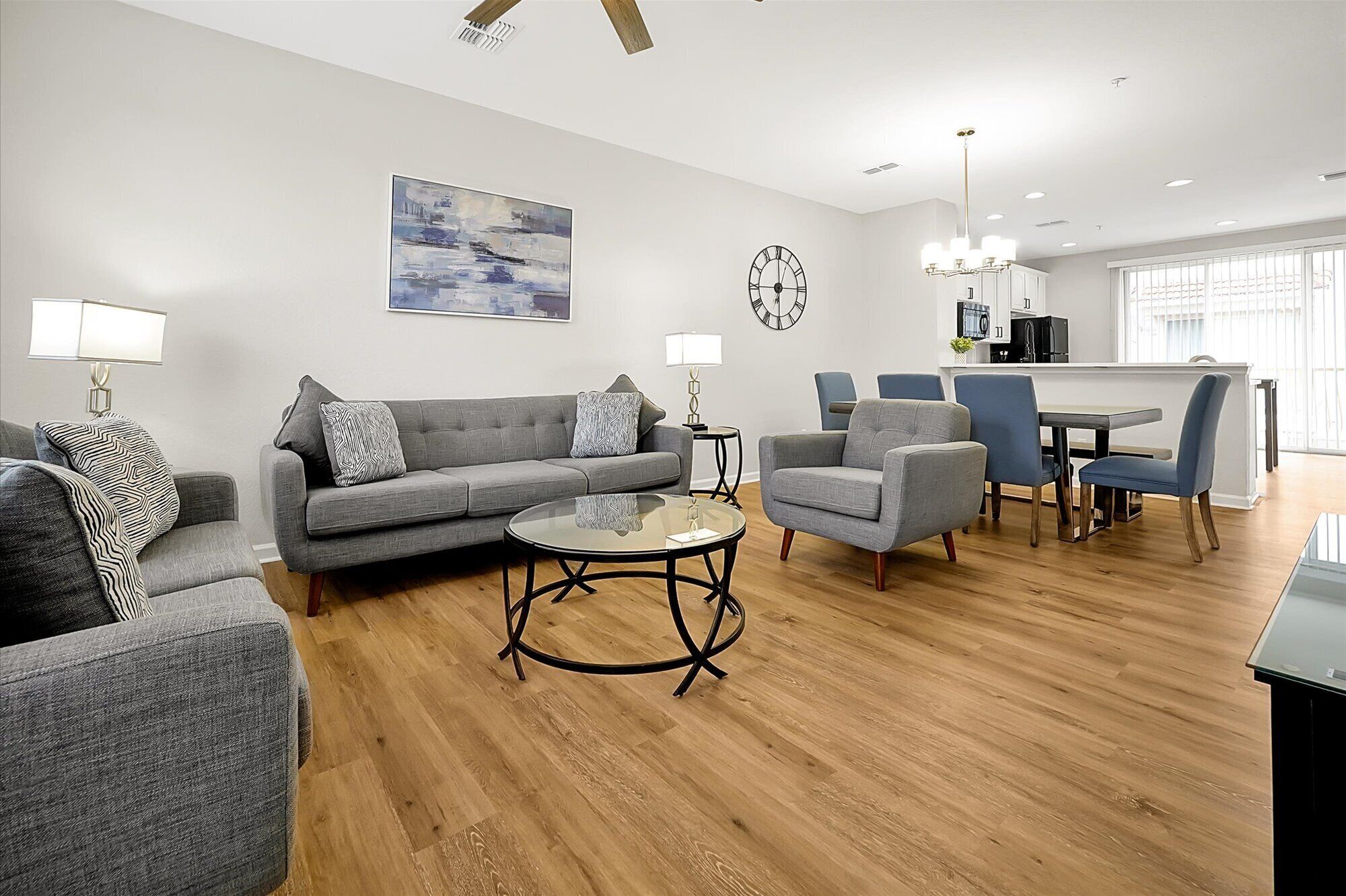 A modern living room with a grey sofa, armchairs, a coffee table, and a dining area with blue chairs and a table.