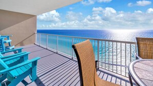 A balcony with a view of the ocean, featuring blue Adirondack chairs and a wicker chair.