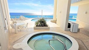 A pool area with a hot tub, lounge chairs, and a view of the ocean.