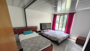 A hotel room with two beds, a nightstand, a lamp, and a window with curtains.