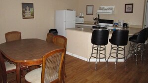 A dining area with a wooden table and chairs, a kitchen with a refrigerator and stove, and a bar area with stools. - Treehouse on the Suwannee River (Mayo)