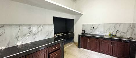 A kitchen with marble backsplash, dark wooden cabinets, and a black countertop.