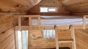 Un intérieur en bois avec un lit superposé, une fenêtre et une échelle.