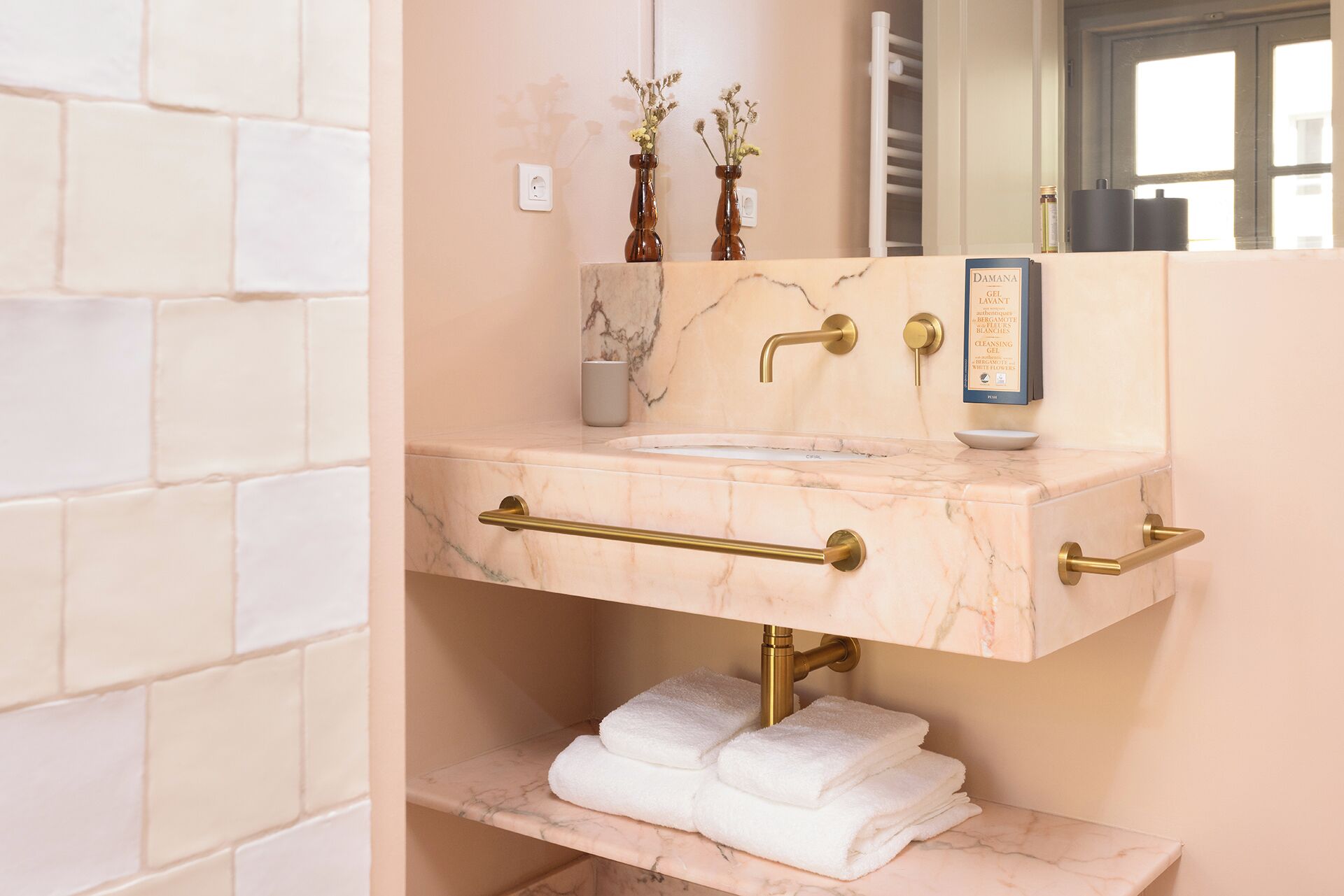 A bathroom with a marble sink, gold fixtures, and a shelf with folded towels.