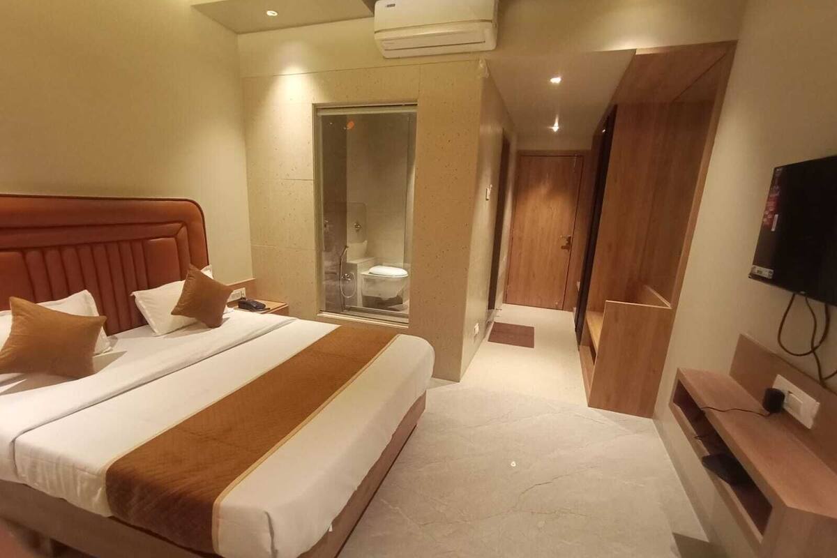 A hotel room with a large bed, a TV, and a bathroom visible through a glass door.
