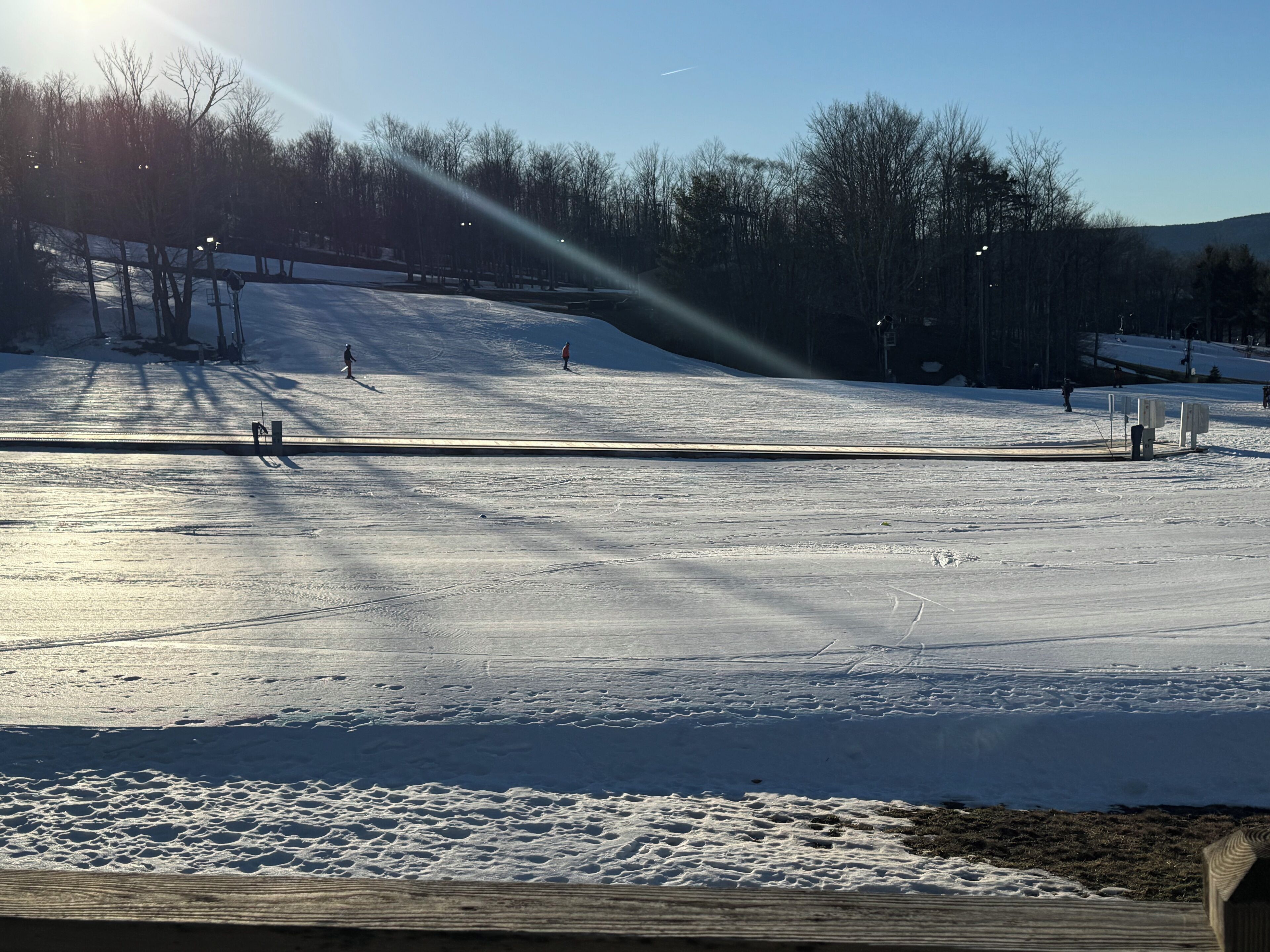A snow-covered ski slope with a wooden viewing platform and a clear sky.
