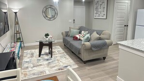 Un salon moderne avec un canapé gris, une table basse en verre, un tapis à motifs et un ventilateur de plafond.