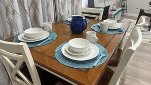 Une table à manger dressée avec de l’assiette blanche, des sets de table bleus et un pichet bleu.