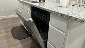 Une cuisine équipée d’un lave-vaisselle intégré, d’un plan de travail en granit et d’une porte blanche à l’arrière-plan.