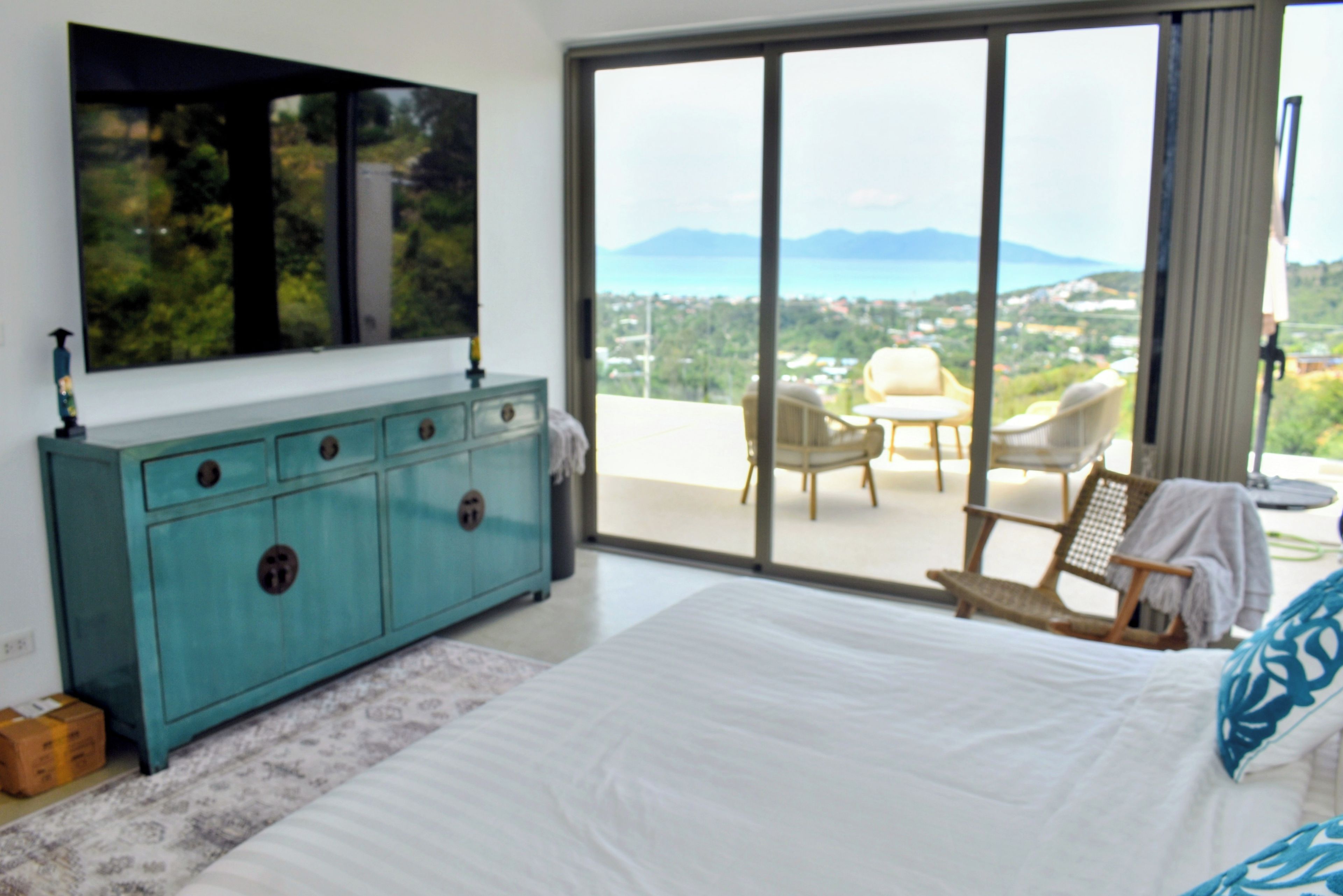 Een slaapkamer met een groot bed, een blauwe dressoir, een televisie en een balkon met uitzicht op het landschap.