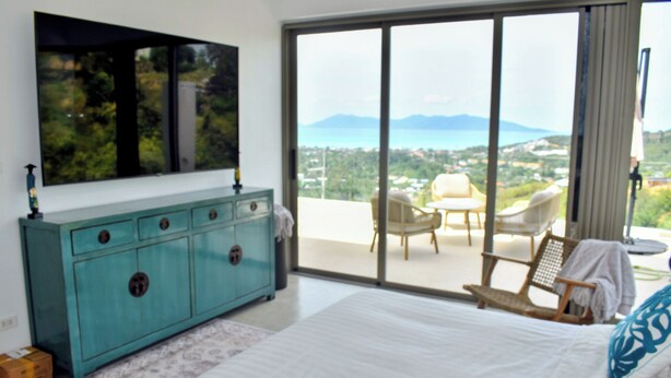 A bedroom with a large bed, a blue dresser, a TV, and a balcony with a view of the landscape. - New single storey villa with sea view, all comforts, close to research area. (Bophut)