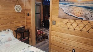 A wooden room with a bed, a painting of a beach, and a door leading to another room. - Charming 1-bedroom house with WiFi, AC on the Bayou in beautiful Bay St. Louis (Bay St. Louis)