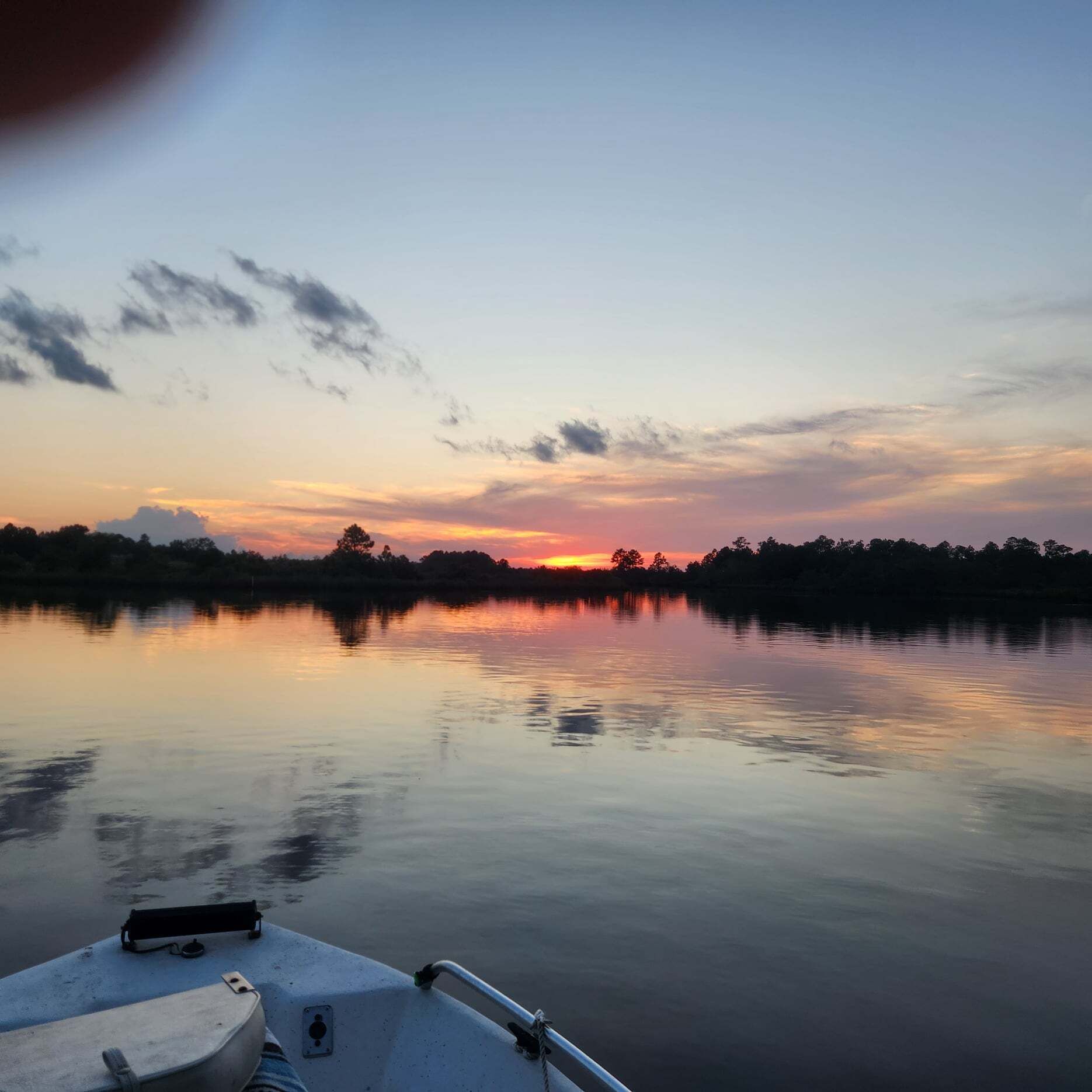 A calm lake at sunset with a boat docked in the foreground.