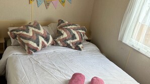 Un llit ben arropat amb almoinades estampades, un moble decoratiu amb espais d'emmagatzematge i una finestra amb cortines translúcides.