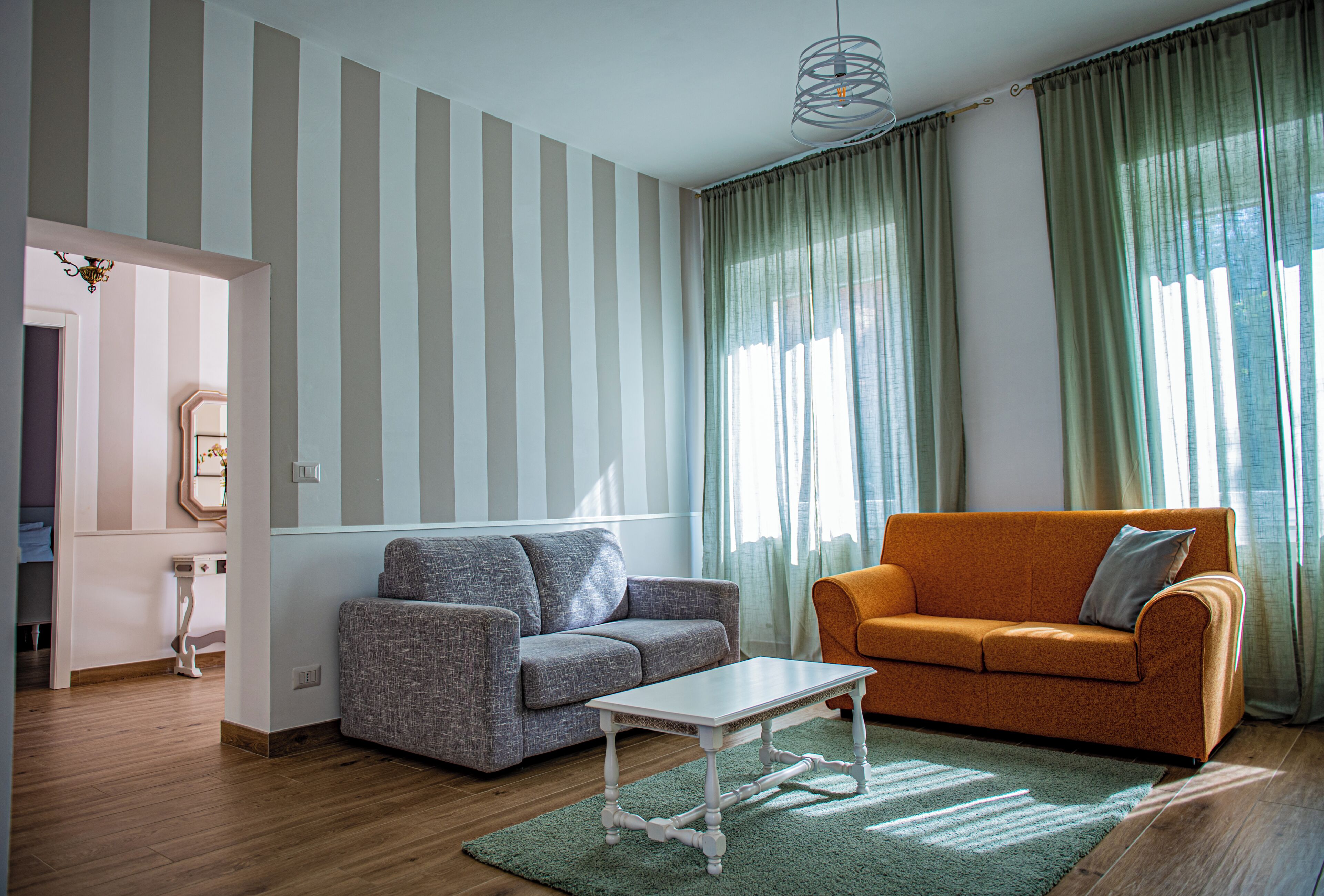 En stue med stribede vægge, en grå sofa, en orange sofa, et hvidt bord og en grøn måtte.
