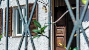Une façade d’immeuble avec une porte en bois et des volets aux fenêtres, une enseigne portant le numéro « 15 », et un petit objet décoratif placé au-dessus de la porte.