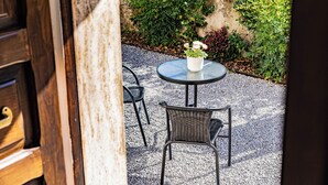 Un espace extérieur aménagé avec une table ronde et deux chaises en osier, entouré de gravier et de verdure.