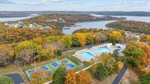 Resort na beira do lago com piscina, quadras de tênis e vista para a floresta e o lago ao redor.